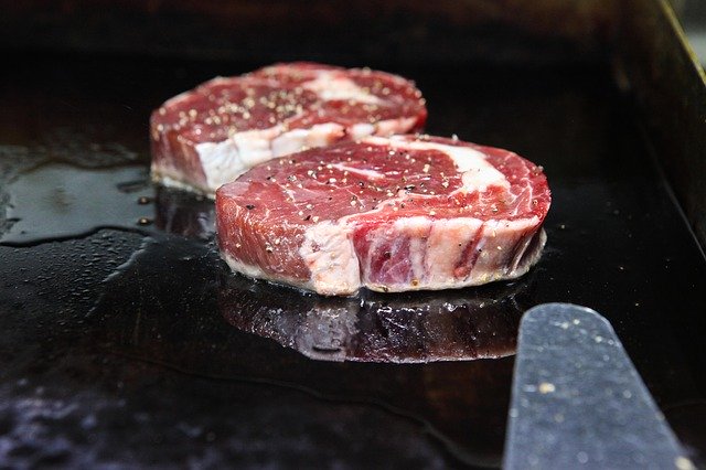鉄板にステーキ肉を乗せて焼いている写真。