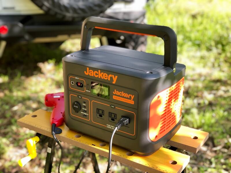 Jackeryポータブル電源1000を実際にキャンプ場で使う、電動ドライバーを接続し、背景に車が写っている。寄りの写真